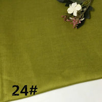 A piece of olive green Colorful Lightweight Ramie Fabric by the yard from Longan Craft is shown, with a small white and pink artificial flower placed in the top right corner and the number 24# printed in black in the bottom left corner.