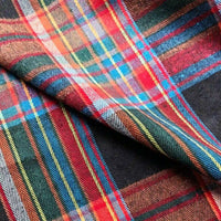 A close-up of Longan Craft’s Colorful One Side Sueded Flannel Fabric By The Yard showcases its super snuggle, yarn-dyed cotton material with a classic plaid pattern in intersecting stripes of red, blue, yellow, green, and white, highlighting the visible texture and folds of this cozy fall flannel.