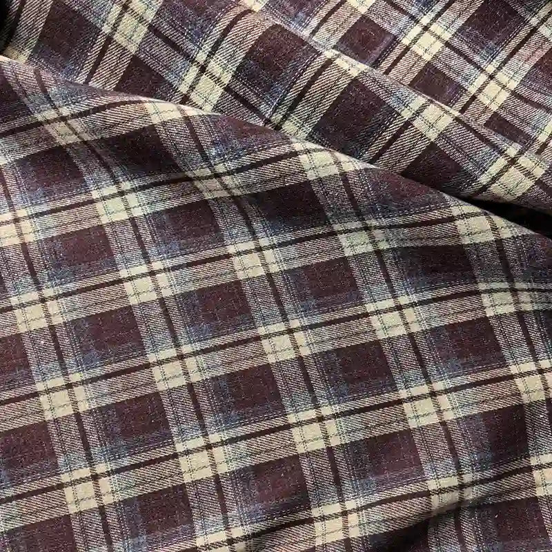 A close-up of the Longan Craft Colorful One Side Sueded Flannel Fabric by the yard showcases its purple and beige yarn dyed cotton plaid design, with intersecting lines forming a classic checkered pattern. The super snuggle fall flannel material appears soft and slightly wrinkled, emphasizing its cozy, sueded texture.