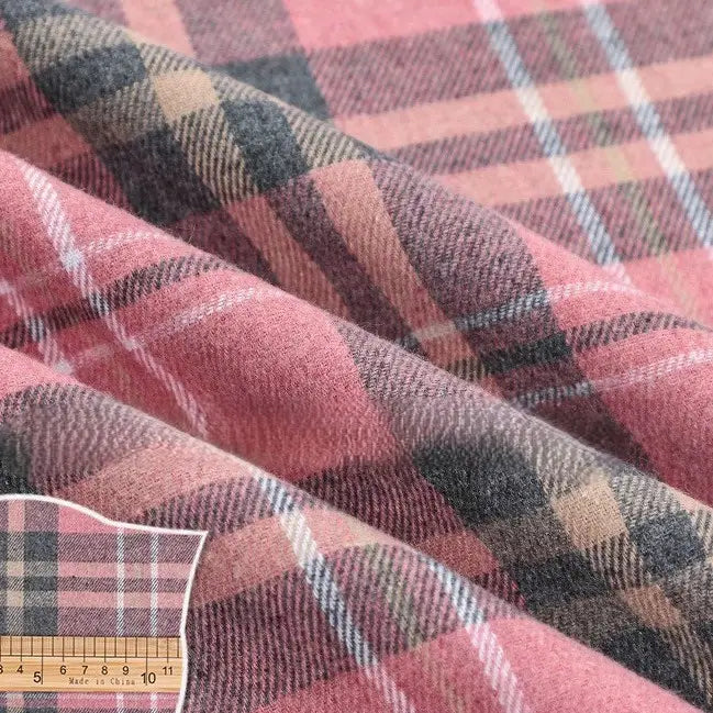 Featuring the Longan Craft Colorful One Side Sueded Flannel Fabric By The Yard, this super snuggle fall material showcases a pink, gray, and beige yarn-dyed cotton plaid pattern. The soft, slightly wrinkled texture highlights its thickness and distinctive weave, with a ruler placed in the corner for scale.