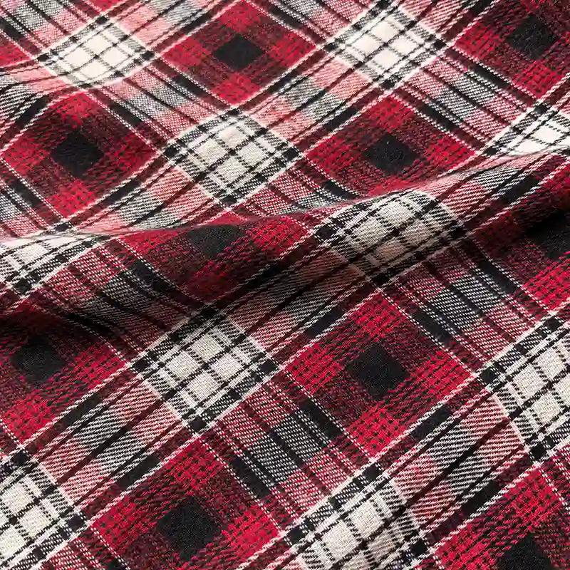 Close-up of the Colorful One Side Sueded Flannel Fabric By The Yard from Longan Craft, featuring a classic red, black, and white yarn-dyed plaid pattern; intersecting lines and squares emphasize its timeless design, while the slightly wrinkled, brushed cotton flannel reveals the super snuggle softness and natural folds of this premium fall material.