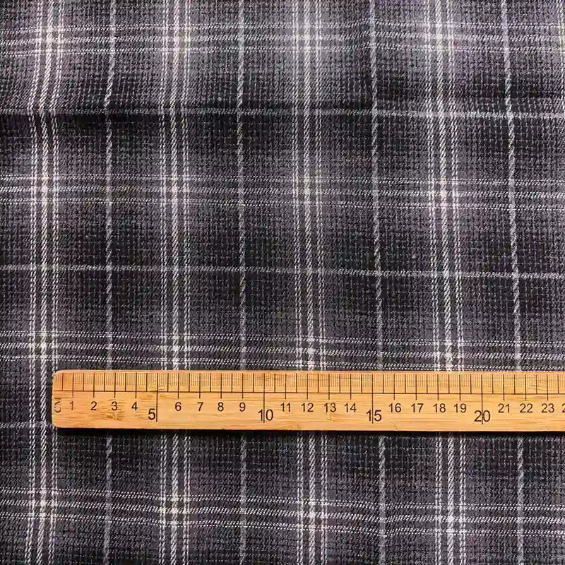 A wooden ruler, marked in centimeters from 0 to 20, is placed on Longan Craft’s Colorful One Side Sueded Flannel Fabric By The Yard—a yarn dyed cotton plaid fabric featuring a dark gray base with white grid lines.