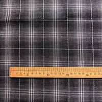 A wooden ruler, marked in centimeters from 0 to 20, is placed on Longan Craft’s Colorful One Side Sueded Flannel Fabric By The Yard—a yarn dyed cotton plaid fabric featuring a dark gray base with white grid lines.