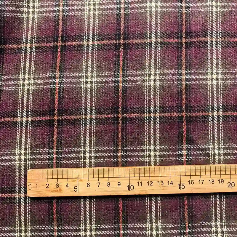 A wooden ruler measuring centimeters is placed on Longan Craft’s Colorful One Side Sueded Flannel Fabric By The Yard, a yarn dyed cotton plaid flannel featuring a super snuggle texture and a purple background with white, yellow, black, and red checkered lines.