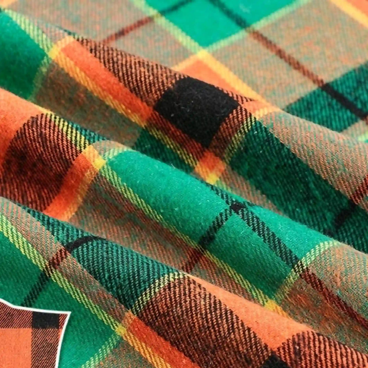 Close-up of folded Colorful One Side Sueded Flannel Fabric By The Yard from Longan Craft, showcasing its vibrant green, orange, black, and yellow plaid pattern and the textured weave of this super snuggle yarn dyed cotton flannel material.
