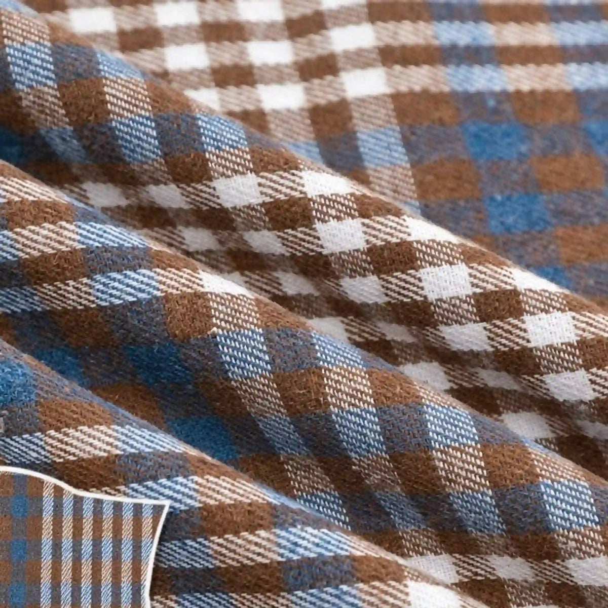 The Colorful One Side Sueded Flannel Fabric by the Yard from Longan Craft features a yarn-dyed cotton plaid design in brown, white, and blue, with a soft sueded finish. Shown here in gentle folds and close-up detail, this Super Snuggle Fall Flannel showcases its woven texture and intersecting checkered lines.