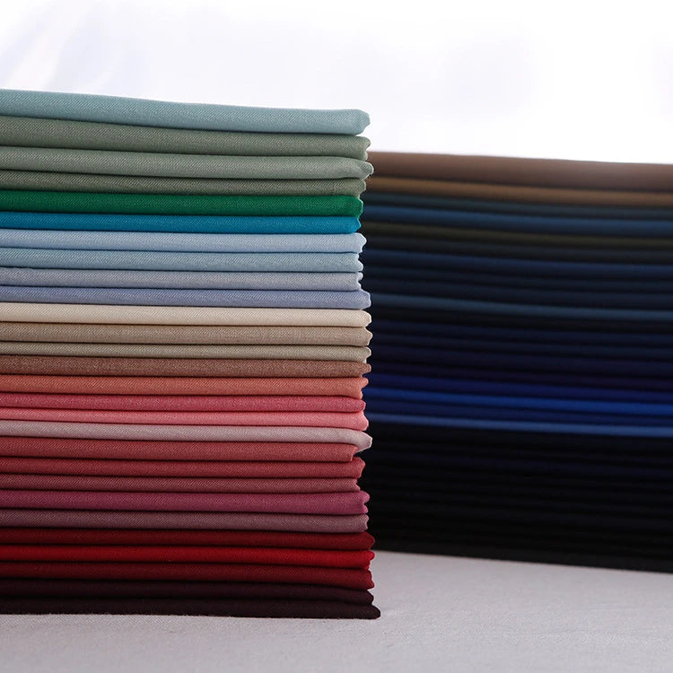 Stacks of Longan Craft Colorful Rayon Polyester Blend Gabardine Fabric by the yard in greens, blues, reds, pinks, neutrals, and dark shades arranged on a white surface—ideal heavyweight viscose material for DIY uniforms.