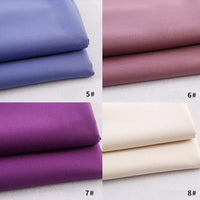 Four folded Longan Craft gabardine fabrics by the yard in light purple, mauve, dark purple, and off-white are stacked on a light background, showcasing the appeal of this colorful rayon polyester blend—perfect for DIY uniforms.