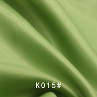 A close-up of smooth, light green Longan Craft satin viscose fabric with gentle folds and a subtle sheen. The text "K015#" appears at the bottom. Ideal for formal dresses, this twill weave material is sold by the yard.