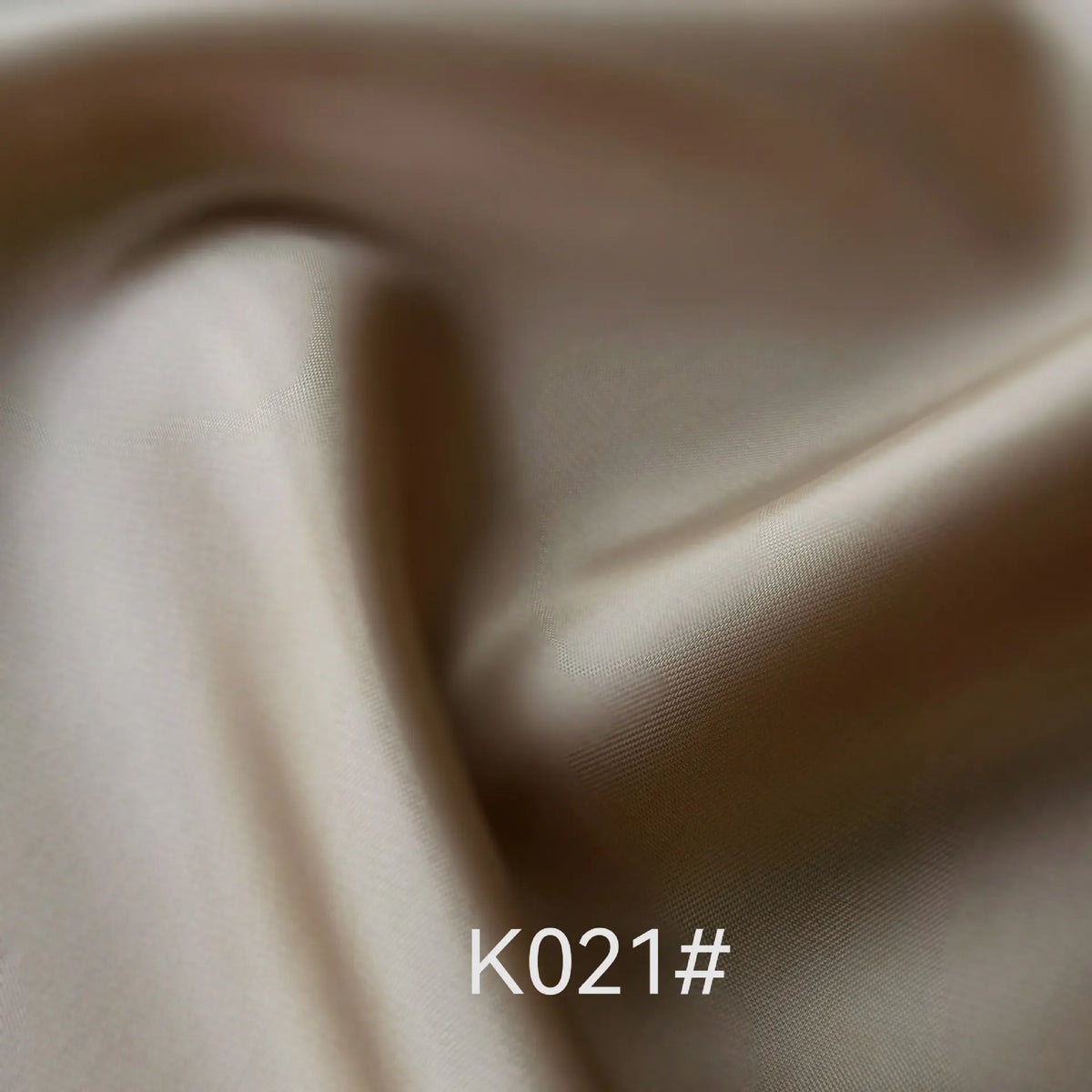 A close-up of smooth, light beige Colorful Satin Viscose Fabric By The Yard from Longan Craft shows gentle folds and a subtle sheen. The text "K021#" appears at the bottom center of the image.