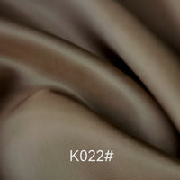 Close-up of Longan Craft’s Colorful Satin Viscose Fabric By The Yard (polyester viscose twill), showing smooth, brown-beige folds under gentle lighting. K022# is displayed at the bottom center of the image. Ideal for formal dresses.