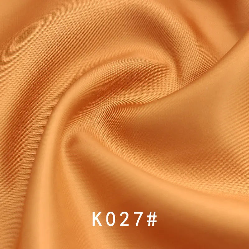 Colorful Satin Viscose Fabric by Longan Craft, in peach-orange with a twill weave and swirling folds; K027# is printed in white at the bottom center—elegant polyester viscose material perfect for formal dresses.