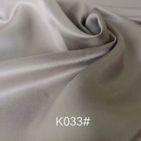 A close-up of elegant, light gray Colorful Satin Viscose Fabric by Longan Craft with gentle folds and a soft sheen. The text K033# appears in white at the bottom, showcasing this twill weave polyester viscose ideal for formal dresses.