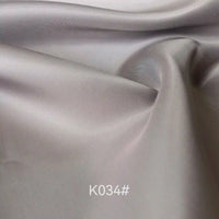 Close-up of light gray, smooth, and slightly shiny Colorful Satin Viscose Fabric By The Yard from Longan Craft, showing gentle folds and creases; polyester viscose twill ideal for formal dresses. Code K034# appears at the bottom center.