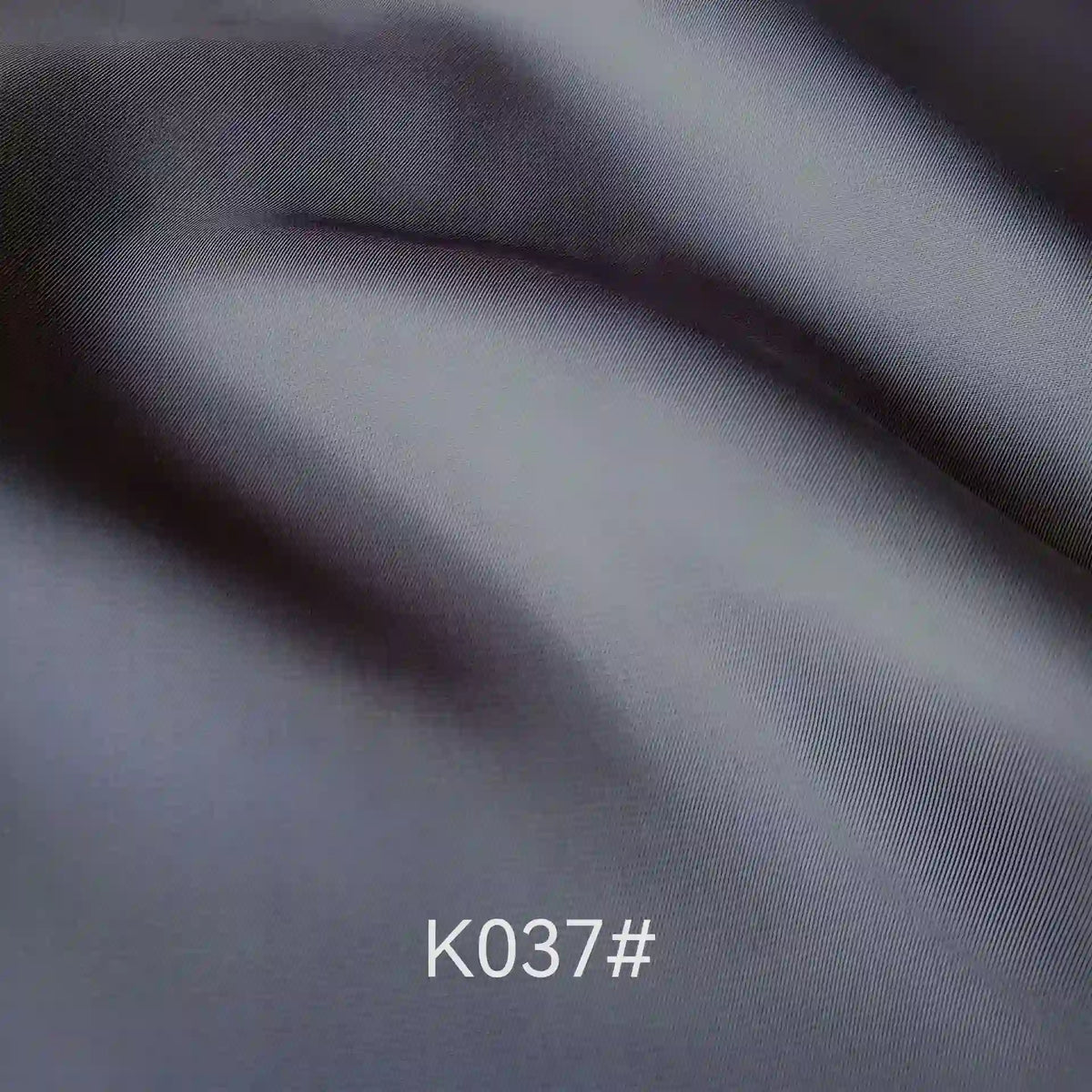 Close-up of smooth, folded gray Colorful Satin Viscose Fabric By The Yard by Longan Craft, showing twill weave with soft shadows and highlights. The code K037# is displayed at the bottom center of the image.