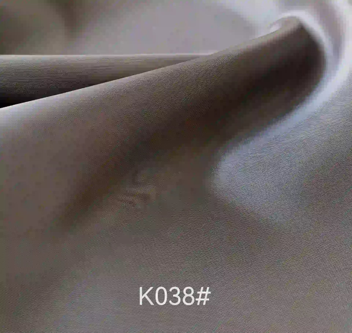 A close-up of smooth, folded grey Longan Craft Colorful Satin Viscose Fabric by the yard, featuring a soft texture and twill weave, code K038# shown at the bottom. Ideal for elegant formal dresses.