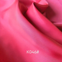 A close-up of smooth, shiny, vibrant pink Colorful Satin Viscose Fabric by Longan Craft with soft folds and "K046#" printed in white at the bottom center; ideal elegant viscose material for formal dresses.