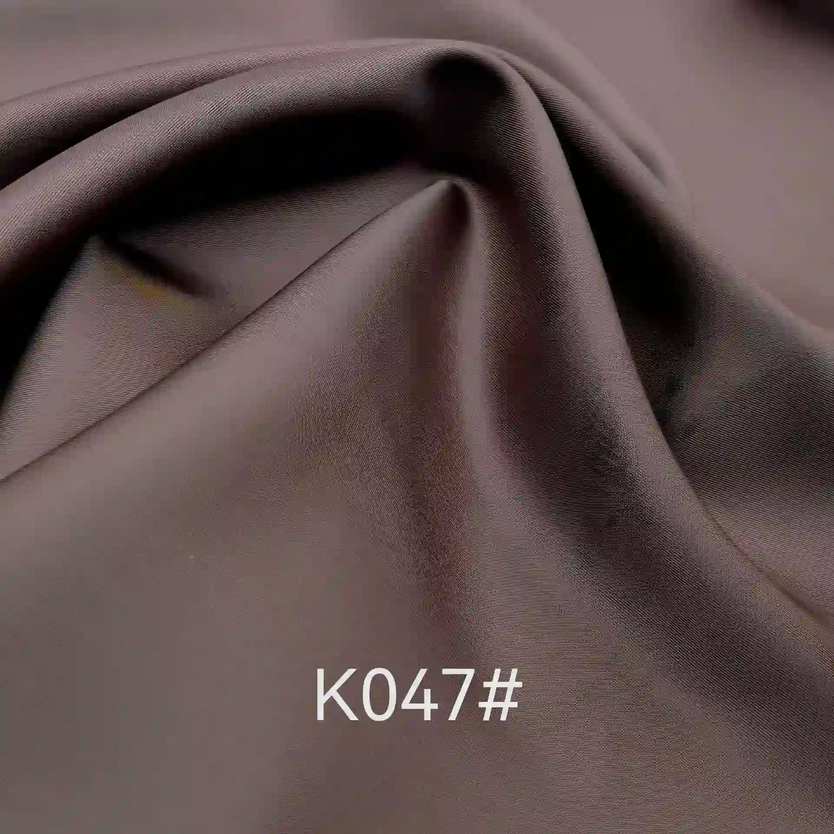 A close-up of Longan Craft's Colorful Satin Viscose Fabric by the yard shows smooth, brown polyester viscose with soft folds and a twill weave. The text K047# appears at the bottom center of the image. Ideal for formal dresses.