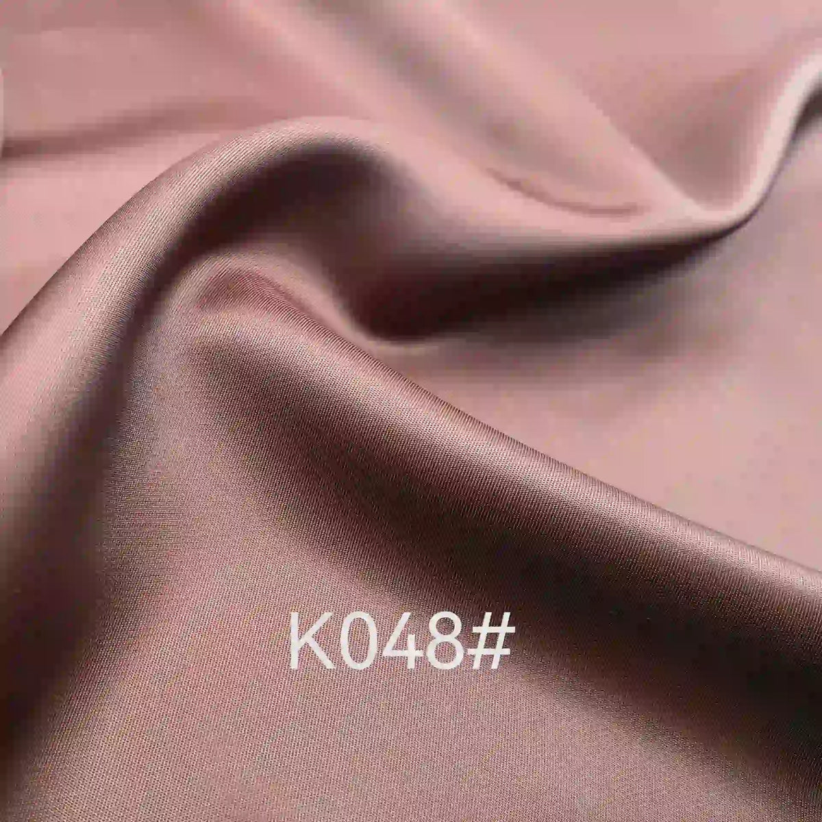 Close-up of smooth, shiny mauve Colorful Satin Viscose Fabric by the Yard from Longan Craft, with twill weave and soft folds—ideal elegant material for formal dresses. “K048#” is printed on its surface.
