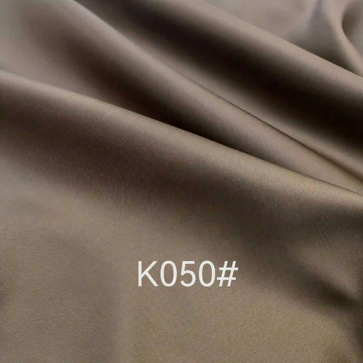 Close-up of smooth, brown Colorful Satin Viscose Fabric By The Yard by Longan Craft. This elegant twill weave polyester viscose material features soft folds and a slight sheen, with "K050#" in white font centered on the fabric.