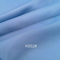 A close-up of smooth, light blue Longan Craft Colorful Satin Viscose Fabric By The Yard shows slight folds and the code K052#, marking this elegant polyester-viscose twill fabric ideal for formal dresses.
