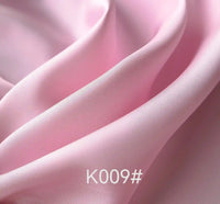 A close-up of Longan Craft Colorful Satin Viscose Fabric By The Yard with a twill weave shows smooth, light pink folds and a satin-like texture. The code K009# appears at the bottom center. Ideal for elegant and formal dresses.