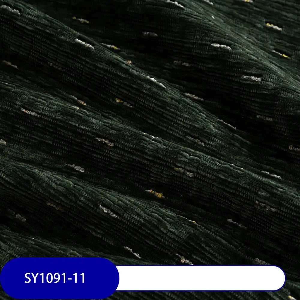 Close-up of Colorful Slub Chenille Fabric by Longan Craft in dark green with ribbed, speckled texture and scattered white and yellow threads. Soft, plush heavyweight chenille for home decor is shown with code SY1091-11 on a blue label.
