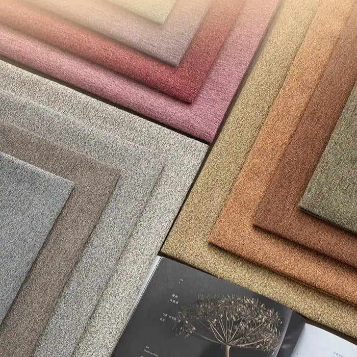 Stacks of Longan Craft Colorful Spot Chenille Fabric by the yard are neatly arranged in muted gray, beige, pink, and brown tones for sofa upholstery or crafts, shown next to an open magazine with a botanical image at the bottom right.