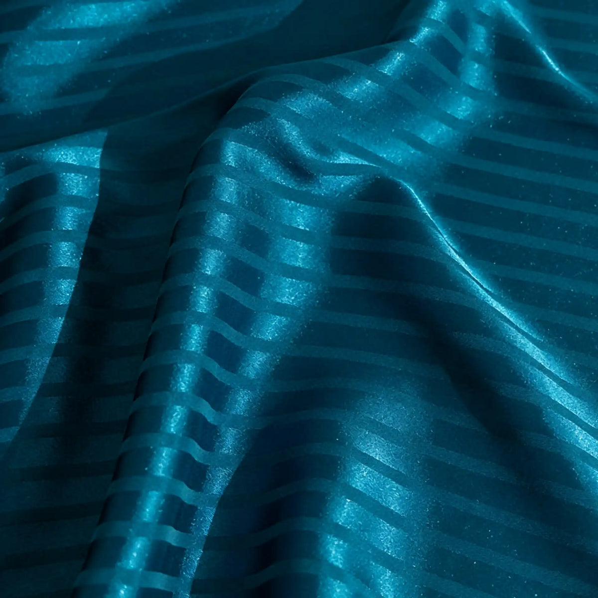 A close-up of Longan Craft’s Colorful Striped Jacquard Satin Fabric shows teal blue diagonal and horizontal stripes, elegant folds, and a smooth, shiny finish—ideal breathable polyester satin material for dressmaking.