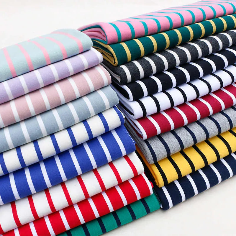 A neatly stacked pile of Longan Craft Colorful Striped Stretch French Terry Fabric By The Yard in pink, green, black, white, blue, red, yellow, and gray is arranged in two rows on a white surface.