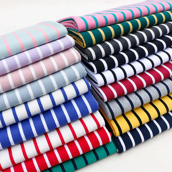 A neatly stacked pile of Longan Craft Colorful Striped Stretch French Terry Fabric By The Yard in pink, green, black, white, blue, red, yellow, and gray is arranged in two rows on a white surface.