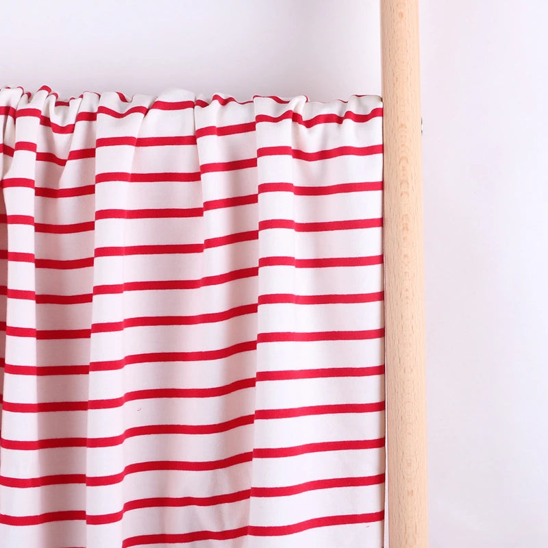 The Colorful Striped Stretch French Terry Fabric by Longan Craft is displayed draped on a wooden rod against a light background, highlighting its vibrant red stripes—perfect knit cotton material for sweatshirts.