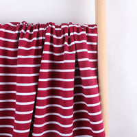 A piece of Longan Craft Colorful Striped Stretch French Terry Fabric, a knit cotton French terry material ideal for sweatshirts, in maroon with white horizontal stripes is draped over a wooden rod against a plain white background.