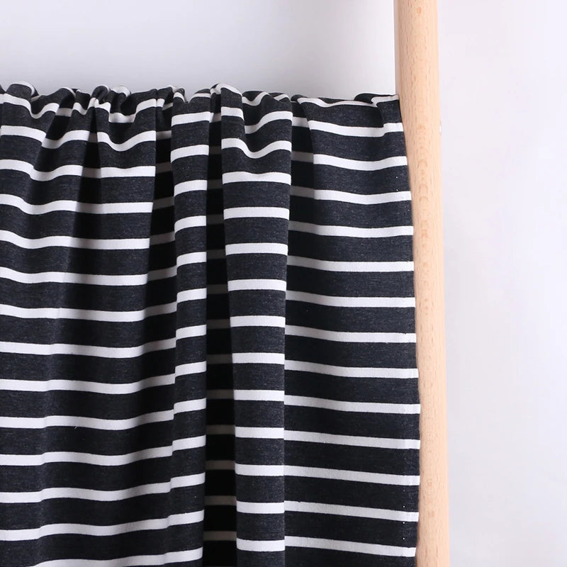 Longan Craft’s Colorful Striped Stretch French Terry Fabric, a knit cotton French terry blend perfect for sweatshirts, is draped over a light wooden rod against a plain background.