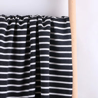 Longan Craft’s Colorful Striped Stretch French Terry Fabric, a knit cotton French terry blend perfect for sweatshirts, is draped over a light wooden rod against a plain background.