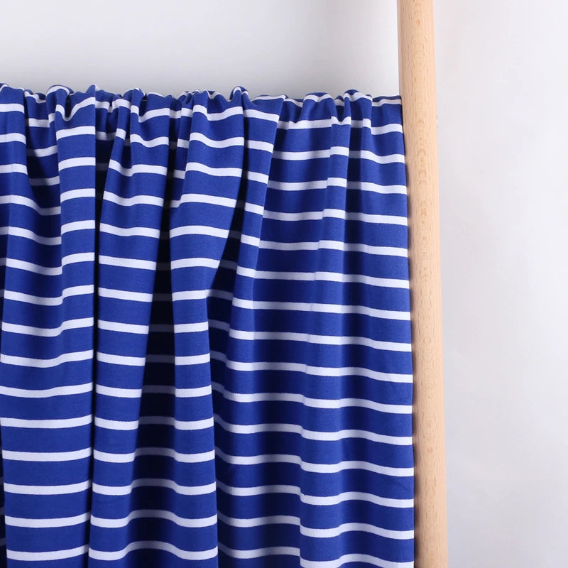 Colorful Striped Stretch French Terry Fabric by Longan Craft, a soft cotton-spandex knit perfect for sweatshirts, is displayed hanging from a light wooden rod against a plain white background.