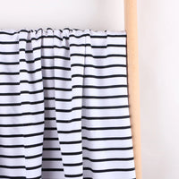The Longan Craft Colorful Striped Stretch French Terry Fabric By The Yard, a knit cotton perfect for sweatshirts, is draped over a light wooden rod against a plain white background.