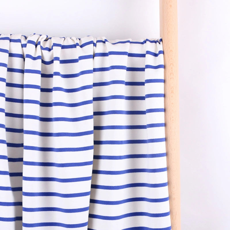A piece of Longan Craft Colorful Striped Stretch French Terry Fabric by the yard, featuring horizontal blue and white stripes, is draped over a light wooden rod against a plain white background. Perfect for sweatshirts.