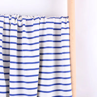 A piece of Longan Craft Colorful Striped Stretch French Terry Fabric by the yard, featuring horizontal blue and white stripes, is draped over a light wooden rod against a plain white background. Perfect for sweatshirts.