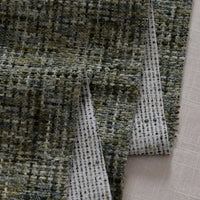 A close-up of Longan Craft's Colorful Tweed Chenille Fabric By The Yard shows its grid-like woven pattern in green, gray, and black shades, draped softly. This textured chenille is ideal for clothing and upholstery.