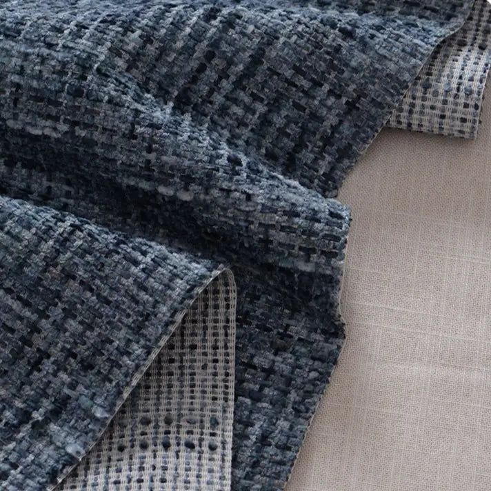 A close-up of Longan Craft’s Colorful Tweed Chenille Fabric By The Yard, featuring a soft, textured blue and gray woven grid pattern draped over smooth beige upholstery fabric—ideal for clothing and décor.