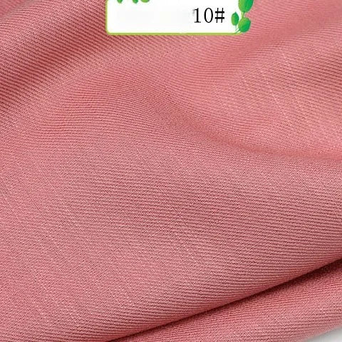 A close-up of Colorful Twill 100 Lyocell Fabric by Longan Craft shows its pink, slightly ribbed texture, with a partial label displaying green text and the number 10#. This sustainable material is ideal for comfortable suits.