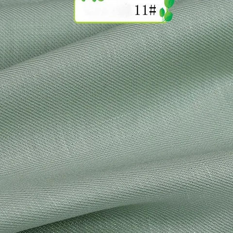 A close-up of light green Colorful Twill 100 Lyocell Fabric by Longan Craft shows smooth, slightly shiny, diagonally textured sustainable material with gentle folds. A partial label with green accents and "11#" appears at the top.