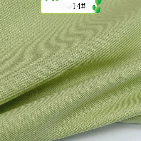 A close-up of Longan Craft's Colorful Twill 100 Lyocell Fabric by the yard, showing its light green hue, subtle textured pattern, and soft flexible drape; a label marked 14# is visible at the top. Sustainable and perfect for suits.