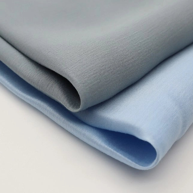 Two pieces of Longan Craft Colorful Viscose Challis Fabric by the yard—lightweight, breathable polyester viscose ideal for sun protection shirts—are neatly folded in light gray and light blue on a white surface.