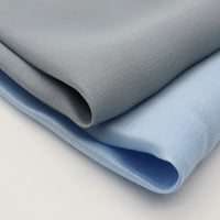 Two pieces of Longan Craft Colorful Viscose Challis Fabric by the yard—lightweight, breathable polyester viscose ideal for sun protection shirts—are neatly folded in light gray and light blue on a white surface.