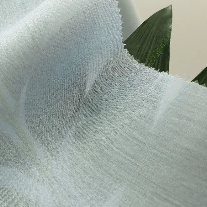A close-up of Longan Craft’s Colorful Viscose Challis Fabric By The Yard, a lightweight, breathable polyester viscose material with a subtle pattern, softly draped over green leaves and ideal for sun protection shirts.