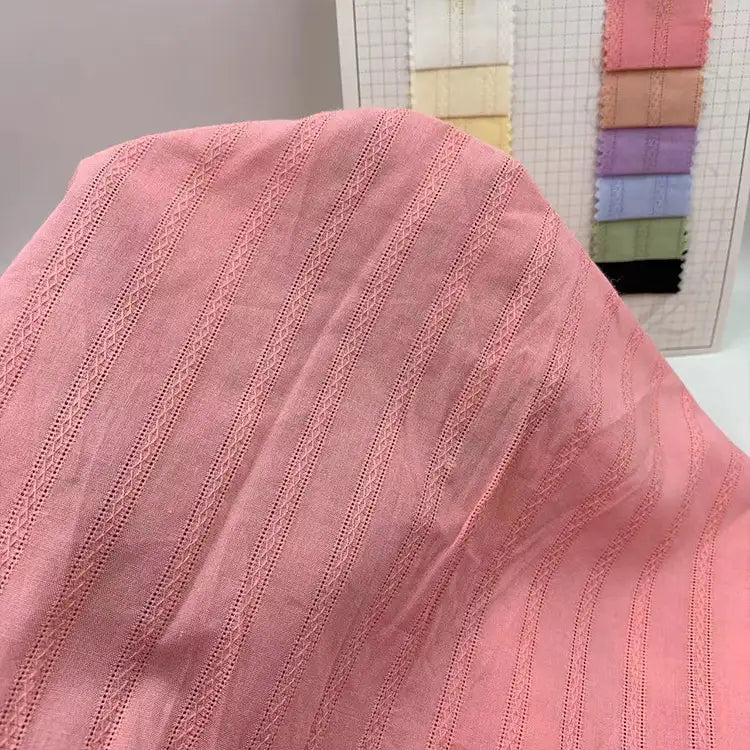A close-up of Longan Craft Colorful Viscose Dobby Fabric by the yard shows light pink cotton-rayon blend with jacquard patterns and fine stripes. Behind it, pastel and neutral swatches are arranged on a white grid color chart.