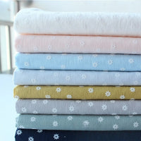 A neatly stacked pile of Longan Craft’s Cotton Floral Printed Voile Fabric By The Yard showcases lightweight, 100% cotton voile in white, pink, blue, yellow, gray, and navy with small white flower prints—perfect for casual wear.