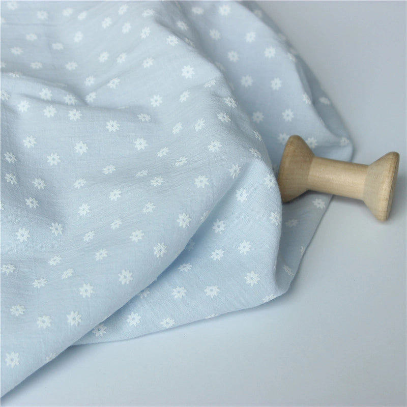 Longan Craft's Cotton Floral Printed Voile Fabric by the yard features a multicolor washed flower print, shown draped beside a wooden spool on a pale surface, perfect as a cozy voile material for casual wear.